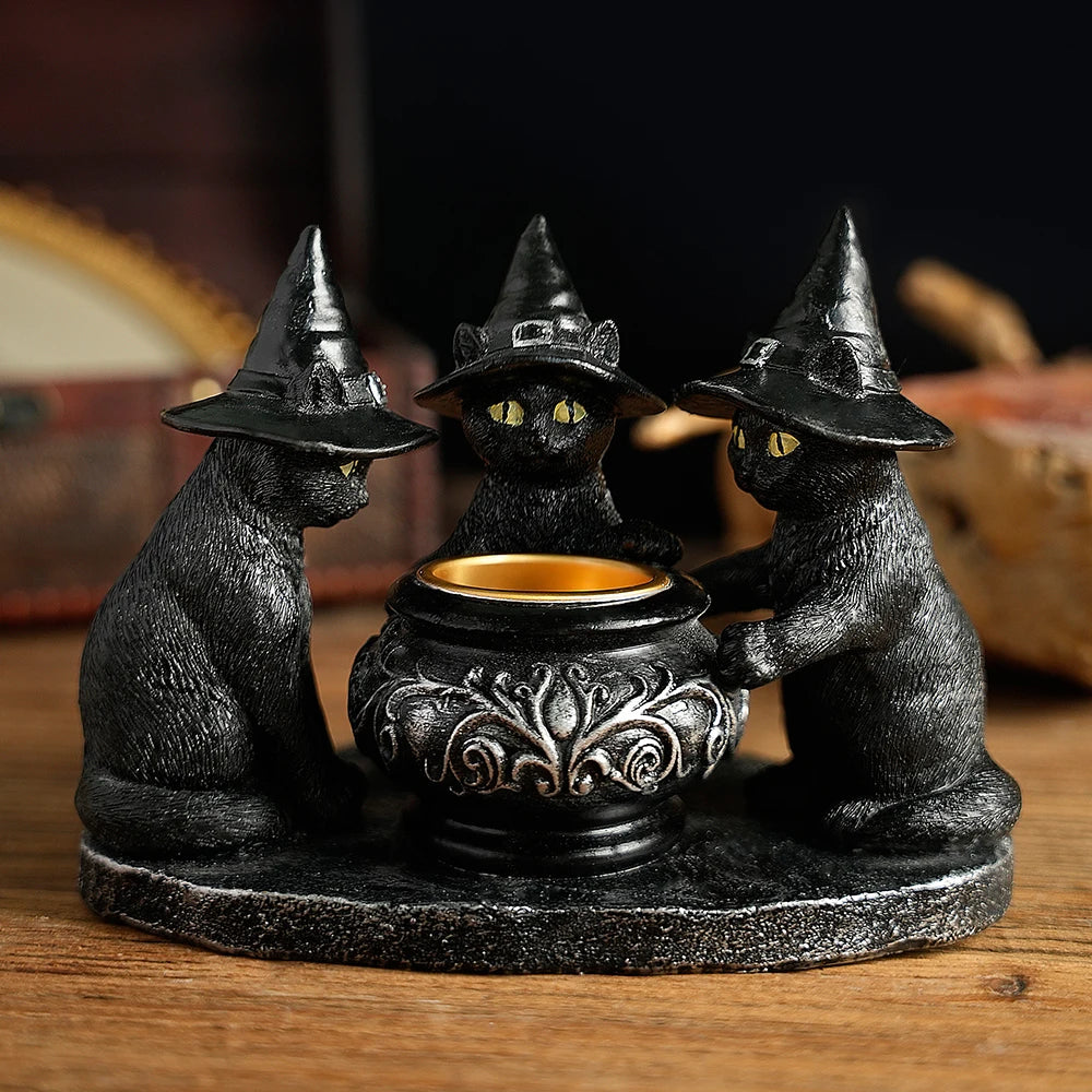 Decorative statue of three cats in witch hats around a cauldron on a wooden surface.